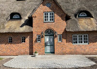 Friesenhaus mit Ziegelfassade und Natursteinpflaster im Eingangsbereich, umgeben von schönem Gartendesign.