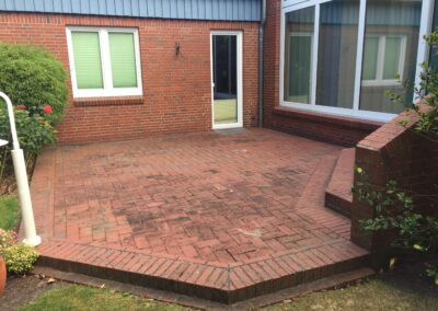 Pflasterung eines Hinterhofs mit roten Ziegelsteinen in einem modernen Garten, inklusive Terrasse mit Stufen, umgeben von Hauswand und Pflanzen